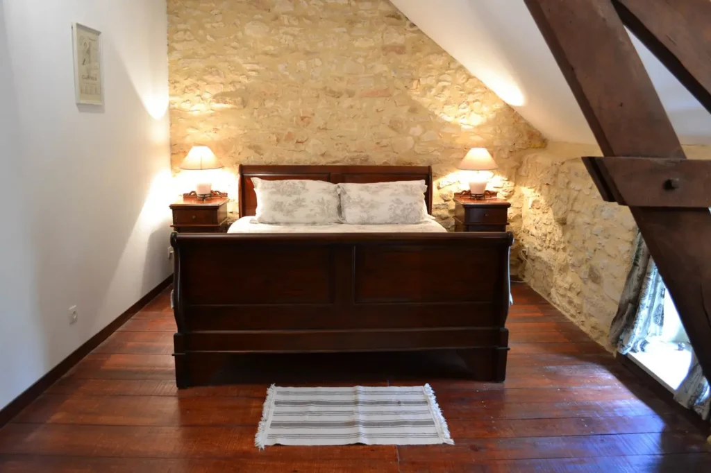 Le lit queen size face au mur de pierre, entre deux lampes de chevet
