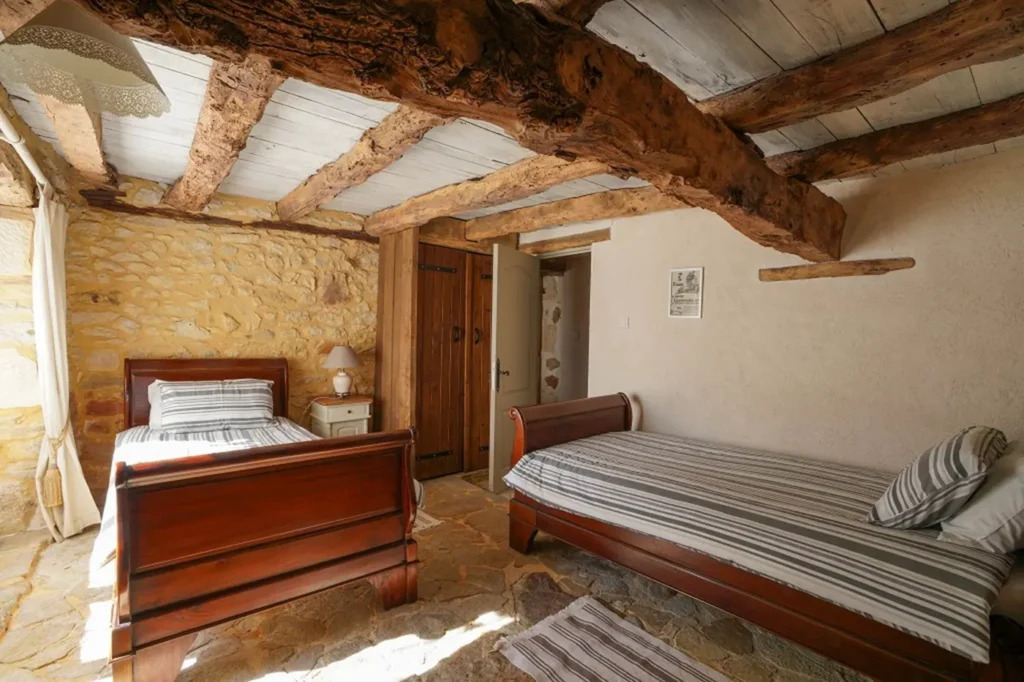 Les deux lits simples en bois et le mur de pierre