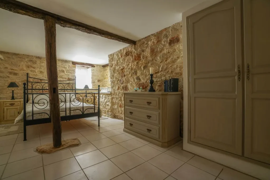 Das Schlafzimmer von La Suite: schmiedeeisernes Bett, Kommode und sichtbarer Holzbalken